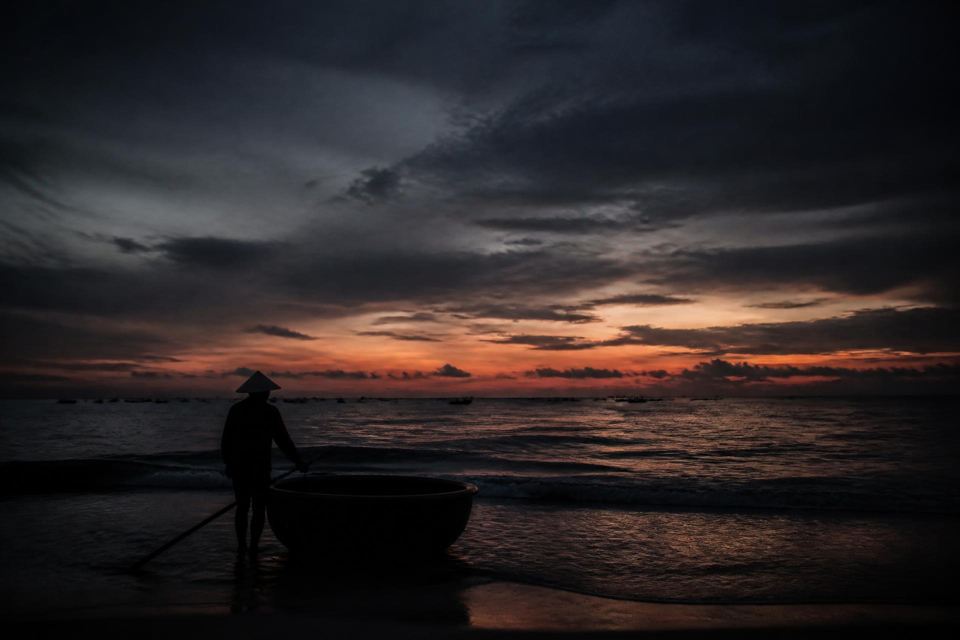 Fisherman with a basket boat on a dark Vietnamese shore at dusk
